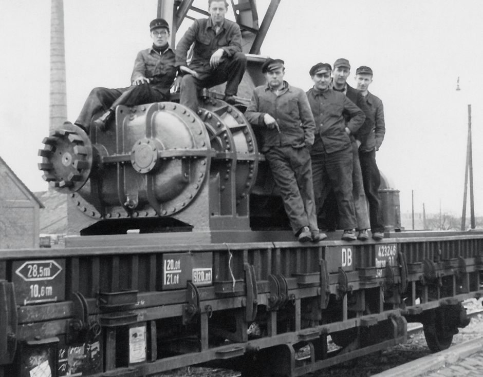 Foto von Mitarbeitern, die auf einem Drehkolbengebläse sitzen, das mit der Bahn nach Berlin transportiert wurde