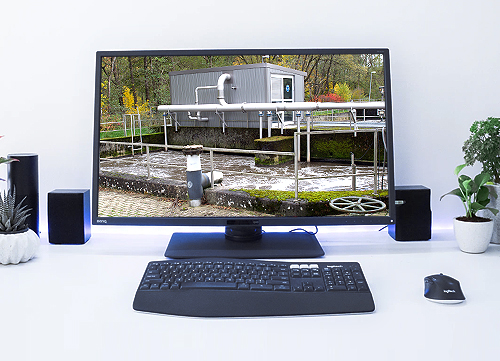 Schreibtisch mit Computermonitor und Tastatur, im Monitor ist ein Klärbecken zu sehen